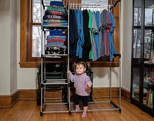 JESSICA LEE / WINNIPEG FREE PRESS

Heather and Sid Barkman&#x2019;s daughter, Penny, 1, is photographed under a rack of their apparel in their Winnipeg home on January 23, 2023. Their two-year-old venture, Maroons Road Apparel, depicts 10 different iconic Winnipeg images on t-shirts, hoodies and prints.

Reporter: Dave Sanderson