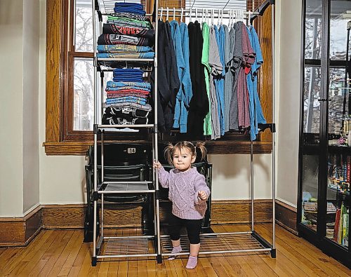 JESSICA LEE / WINNIPEG FREE PRESS

Heather and Sid Barkman&#x2019;s daughter, Penny, 1, is photographed under a rack of their apparel in their Winnipeg home on January 23, 2023. Their two-year-old venture, Maroons Road Apparel, depicts 10 different iconic Winnipeg images on t-shirts, hoodies and prints.

Reporter: Dave Sanderson