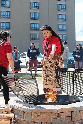 Attendees of Friday's Red Dress Day ceremony at Brandon University drop some tobacco in the ceremonial fire to commemorate murdered and missing Indigenous women and girls. (Kyle Darbyson/The Brandon Sun) 