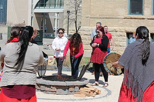 Attendees of Friday's Red Dress Day ceremony at Brandon University drop some tobacco in the ceremonial fire to commemorate murdered and missing Indigenous women and girls. (Kyle Darbyson/The Brandon Sun) 