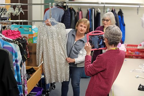 Eileen Mosson holds up a dress while Marlene Brichon takes a photo with an iPad to post on the Nearly New Shop's Facebook page on Tuesday. Barb Barrie looks on in the background. The ladies are members of the Brandon Regional Health Centre (BRHC) Auxiliary. (Michele McDougall/The Brandon Sun)