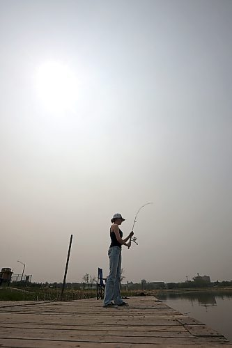 Phoenix Jackson fishes from the dock on the Assiniboine River at Dinsdale Park earlier this month under smoke-filled skies. (Tim Smith/The Brandon Sun)