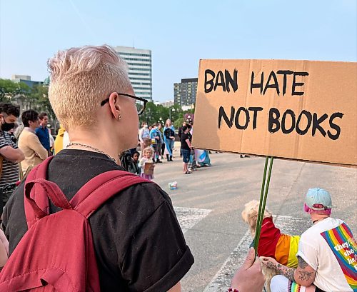 Ash Laing holds up a protest sign on the Manitoba Legislative Building grounds in protest of book banning requests on Tuesday, May 23, 2023. (Maggie MacIntosh / Winnipeg Free Press)