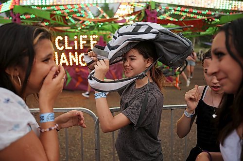 Olivia Relf uses a friend’s backpack to shield herself from the rain while waiting in line for a midway ride during the opening night of the 2023 Manitoba Summer Fair at the Keystone Centre grounds on a hot and stormy Wednesday night. More photos on Page A3. (Tim Smith/The Brandon Sun)