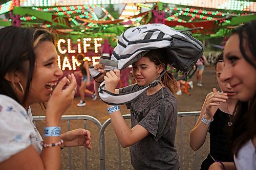 07062023
Olivia Relf uses a friend&#x2019;s backpack to shield herself from the rain while waiting in line for a midway ride during the opening night of the 2023 Manitoba Summer Fair at the Keystone Centre on a hot and stormy Wednesday night. (Tim Smith/The Brandon Sun)