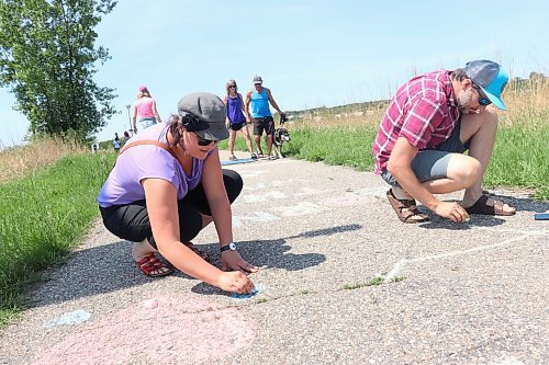 Steffi Lazerte and Alex Koiter write queer positive aphorisms in chalk on the Riverbank Discovery Centre walkway Sunday afternoon to help celebrate the beginning of Brandon Pride Week. (Kyle Darbyson/The Brandon Sun)