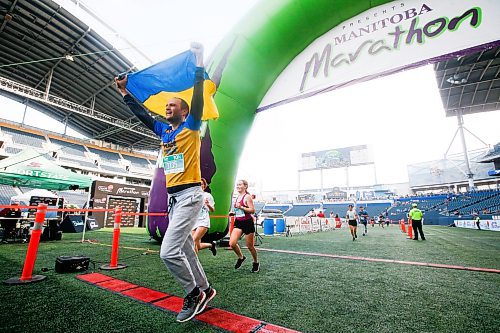 JOHN WOODS / WINNIPEG FREE PRESS
Ilya Vakurov, carrying a Ukraine flag, finishes the 45th Manitoba Marathon in Winnipeg, Sunday, June 18, 2023. 

Reporter: Donald