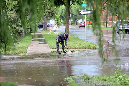 Local resident Gord Dupuis cleans out a clogged storm grate at the corner of 14th Street and Louis Avenue on Tuesday afternoon, following a massive thunderstorm that flooded several streets in the city. (Matt Goerzen/The Brandon Sun)