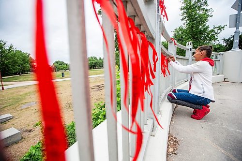 MIKAELA MACKENZIE / WINNIPEG FREE PRESS

Diane Bousquet ties red ribbons with the names of missing and murdered Indigenous women onto the railing at the Louis Riel Bridge by Camp Marcedes on Wednesday, July 19, 2023. For Chris story.
Winnipeg Free Press 2023.