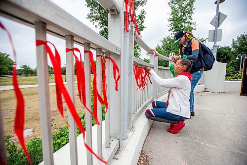 MIKAELA MACKENZIE / WINNIPEG FREE PRESS

Diane Bousquet (left) and Melanie Berestin tie red ribbons with the names of missing and murdered Indigenous women onto the railing at the Louis Riel Bridge by Camp Marcedes on Wednesday, July 19, 2023. For Chris story.
Winnipeg Free Press 2023.