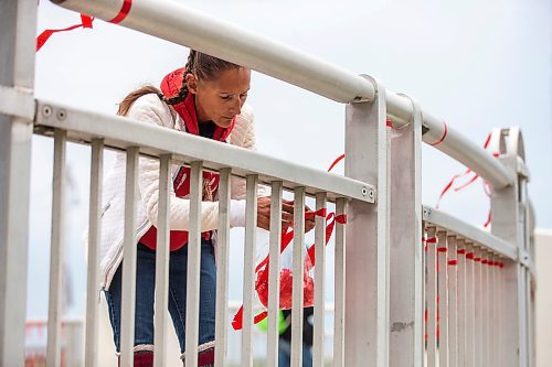 MIKAELA MACKENZIE / WINNIPEG FREE PRESS

Diane Bousquet ties red ribbons with the names of missing and murdered Indigenous women onto the railing at the Louis Riel Bridge by Camp Marcedes on Wednesday, July 19, 2023. For Chris story.
Winnipeg Free Press 2023.