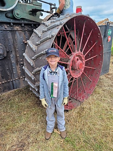 Seven-year-old Noah Beamish stands in front of his family's 1913 75 Case 75-HP steam traction engine while his uncle Andrew Beamish works on it. (Miranda Leybourne/The Brandon Sun)