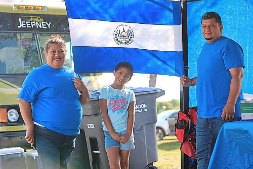 The Rodriguez family, including Jackie, Mia and Oscar, pose for a photo in front of the flag of El Salvador as they set up their booth for the celebration. (Kyle Darbyson/The Brandon Sun)