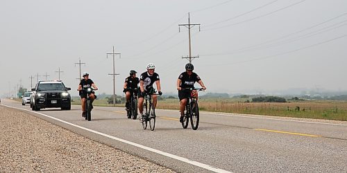 Shilo soldier Rob Nederlof in front, rides beside Cst. Amanda Conway, and two other members of Brandon Police Service Cst. Selena Samagalski, Cst. Meghan Puteran, with Cst. Dufault in the BPS police cruiser on the Trans Canada Highway on Tuesday. Nederlof is cycling 1,000 kms to raise funds and awareness for the Wounded Warrior PTSD Service Dogs program. (Michele McDougall/The Brandon Sun)