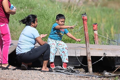 Four-year-old Charles Asejo throws rocks into the water on the shore of the Souris River from his perch on a dock on Wednesday afternoon. His mother Charlot Asejo and his grandmother Esdrella Noble regularly take the youngster to the riverbank in Souris's Victoria Park to get some and enjoy the view.  (Matt Goerzen/The Brandon Sun)