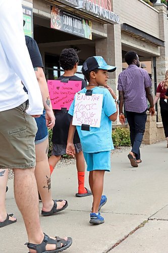 Seven-year-old Zawadi Nundu, sporting a sign on his back that reads &quot;End the toxic drug supply&quot; walks with his family along Victoria Avenue to mark International Overdose Awarness Day on Wednesday afternoon. (Matt Goerzen/The Brandon Sun)