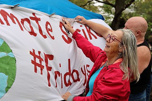 Rae Smith and Rune Wolf hang a banner during the Global Climate Strike event in Brandon's Princess Park on Friday. (Michele McDougall/The Brandon Sun)
