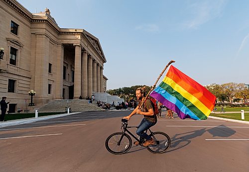 MIKE DEAL / WINNIPEG FREE PRESS
Trans Rights supporter, Christian Bethge, rides his bike while flying a rainbow flag at the Manitoba Legislative building Wednesday morning.
230920 - Wednesday, September 20, 2023.