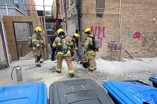 A Brandon firefighter spreads out burning garbage at the south end brick wall of the Laplont block on Wednesday afternoon in downtown Brandon. Emergency crews, including Brandon police and fire, attended the scene of a garbage fire that appeared to have spread to a back gate of the property. (Matt Goerzen/The Brandon Sun)