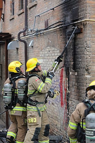 A Brandon firefighter pulls a burned wooden frame from the south end brick wall of the Laplont block on Wednesday afternoon. Emergency crews, including Brandon police and fire, attended the scene of a garbage fire that appeared to have spread to a back gate of the property. (Matt Goerzen/The Brandon Sun)