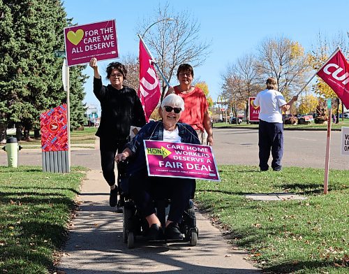 Helen Janzen, a resident of Valleyview Extendicare, is wheeled down the sidewalk alongside support staff carrying a sign that said "Care home workers deserve a fair deal" on Friday. (Michele McDougall/The Brandon Sun)