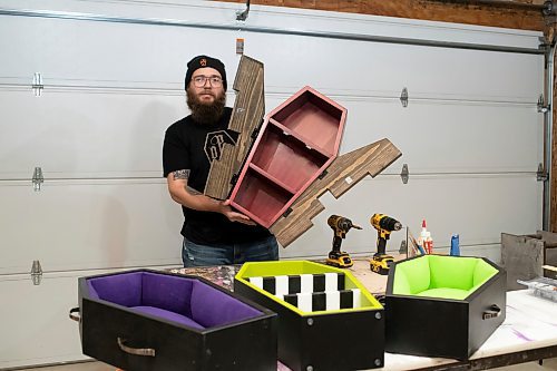 BROOK JONES / WINNIPEG FREE PRESS
Blake Locken, who works as a carpenter by day, runs a home-based business called Old Pine Box Curiousitiies. Locken is pictured holding a coffin shaped cabinet in his garage, which dubs as his workshop, in Winnipeg, Man., Wednesday, Oct. 11 . He also builds upholstered pet beds and charcuterie boards, all with a coffin shape theme. The Winnipeg resident will be a vendor at the Punk Rock Flea Market at the University of Manitoba in Winnipeg, Man., Saturday, Oct. 14, 2023 from 10:30 a.m. to 5 p.m. The event also run Sunday, Oct. 15, 2023.