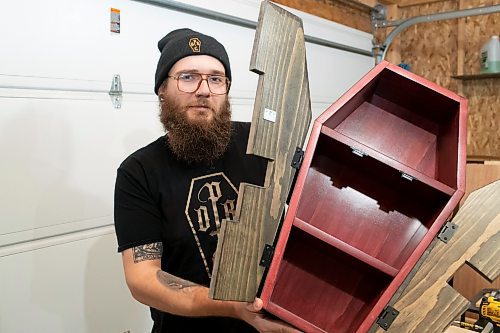 BROOK JONES / WINNIPEG FREE PRESS
Blake Locken, who works as a carpenter by day, runs a home-based business called Old Pine Box Curiousitiies. Locken is pictured holding a coffin shaped cabinet in his garage, which dubs as his workshop, in Winnipeg, Man., Wednesday, Oct. 11 . He also builds upholstered pet beds and charcuterie boards, all with a coffin shape theme. The Winnipeg resident will be a vendor at the Punk Rock Flea Market at the University of Manitoba in Winnipeg, Man., Saturday, Oct. 14, 2023 from 10:30 a.m. to 5 p.m. The event also run Sunday, Oct. 15, 2023.