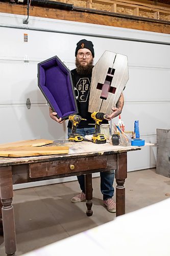 BROOK JONES / WINNIPEG FREE PRESS
Blake Locken, who works as a carpenter by day, runs a home-based business called Old Pine Box Curiousitiies. Locken is pictured holding a coffin-shaped pet bed as well as a coffin shaped cabinet in his garage, which dubs as his workshop, in Winnipeg, Man., Wednesday, Oct. 11. He also builds charcuterie boards, coffee tables, book shelves and wine racks. The Winnipeg resident will be a vendor at the Punk Rock Flea Market at the University of Manitoba in Winnipeg, Man., Saturday, Oct. 14, 2023 from 10:30 a.m. to 5 p.m. The event also run Sunday, Oct. 15, 2023.