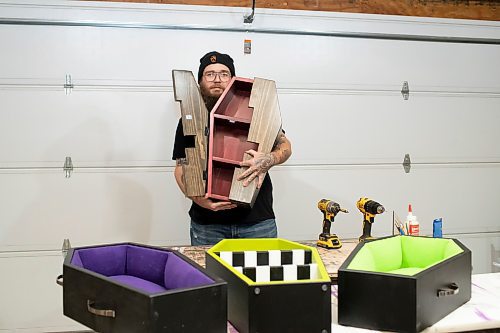 BROOK JONES / WINNIPEG FREE PRESS
Blake Locken, who works as a carpenter by day, runs a home-based business called Old Pine Box Curiousitiies. Locken is pictured holding a coffin shaped cabinet in his garage, which dubs as his workshop, in Winnipeg, Man., Wednesday, Oct. 11. He also builds upholstered pet beds and charcuterie boards, all with a coffin shape theme. The Winnipeg resident will be a vendor at the Punk Rock Flea Market at the University of Manitoba in Winnipeg, Man., Saturday, Oct. 14, 2023 from 10:30 a.m. to 5 p.m. The event also run Sunday, Oct. 15, 2023.