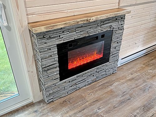 Photos by Marc LaBossiere / Winnipeg Free Press
An electric wall-mount fireplace is recessed within a structure sheathed in faux-stone, topped with a live-edge wooden mantle.
 