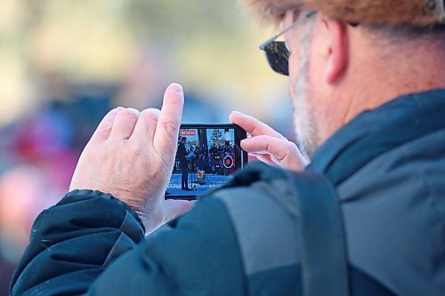 A member of the audience for the No Stone Left Alone ceremony at the Brandon Municipal Cemetery uses their phone to record a message offtered by Special Envoy for Military Affairs Minister David Pankratz on Friday morning. (Matt Goerzen/The Brandon Sun)