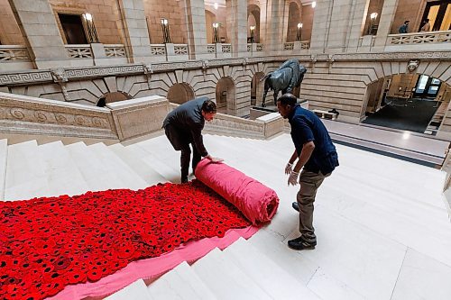 MIKE DEAL / WINNIPEG FREE PRESS
Manitoba Legislative building maintenance staff, Tesfay Fanta (right) and Brad Robertson (left), Manitoba&#x2019;s Chief of Protocol, unroll a section of the Poppy Blanket, Monday morning.
First unveiled in November of 2019 the Poppy Blanket is an 85 foot long collection of over 8000 handmade poppies and thousands of dedicated ribbons. It was made in less than a year between 2018 and 2019 by the Handmade Winnipeg Facebook group community.
231106 - Monday, November 06, 2023.