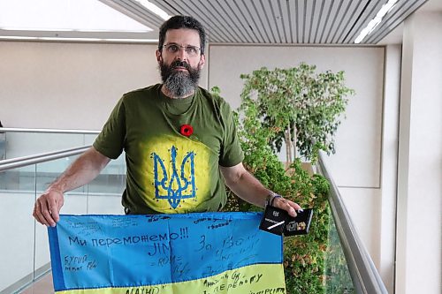 Peter Derksen stands in the atrium of the Winnipeg Free Press building holding a flag signed by Ukrainian soldiers and a medal given to him by military officials. Derksen, a retired Winnipeg Police Service member, enlisted with the Ukrainian military and spent a year fighting in the southeast region of Ukraine. (Tyler Searle / Winnipeg Free Press)