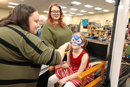 L-R: Lavender Blue Henna & Face Painting owner Stephanie Ritchot making Sonic design on Liliana Larocque-Shurb, 5, while her mum, Taylor Shurb, watches at the Christmas Market on Saturday. Photo: (Abiola Odutola/The Brandon Sun)