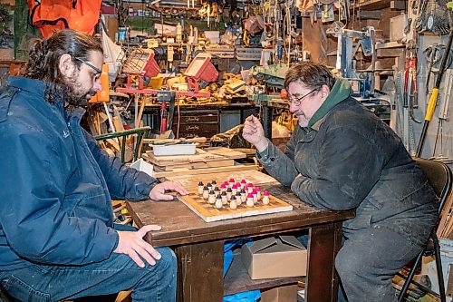 BROOK JONES / WINNIPEG FREE PRESS
Sixty-seven-year-old Bill Gidzak and his son 42-year-old son Nick run a woodworking shop called Artisanal Firewood. The father-and-son team turn out a variety of products, especially Christmas theme decorations and toys for kids. Pictured: Nick (left) and his father Bill play a game of checkers on a board and with pieces they handmade. The board is made of oak wood and the pieces are made of maple wood. The duo were pictured woodworking inside Bill's garage at his home in Winnipeg, Man., Wednesday, Nov. 22, 2023.