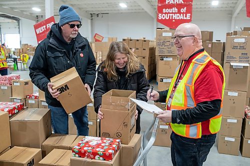 BROOK JONES / WINNIPEG FREE PRESS
Terry Sharman (right) volunteers as a Christmas hamper checker while Garth Dow (left) and his wife Glenis Dow (middle) pick up Christmas hampers ready for delivery. The trio were pictured at the Christmas Cheer Board at 895 Century St., in Winnipeg, Man., Friday, Dec. 15, 2023.  The Dows have been voluntering for the Christmas Cheer Board for a few years, however, it's the couiple's first time volunteering as delivery drivers.