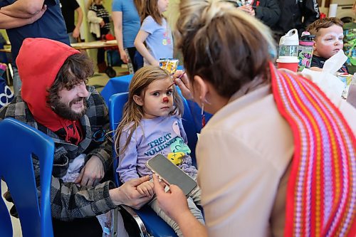 Madeleine Erickson sits patiently with her dad Tyler at her side, while volunteer Nichelle Wilk paints her face, during Louis Riel Day celebrations at the Manitoba Métis Federation’s southwest region’s building in Brandon on Monday. (Michele McDougall/The Brandon Sun)  