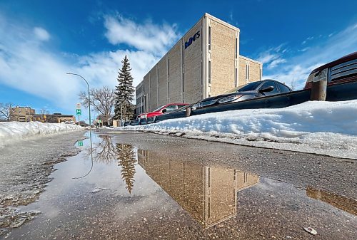 Meltwater on the sidewalk reflects Brandon's BellMTS building on 18th Street on Monday afternoon. (Matt Goerzen/The Brandon Sun)