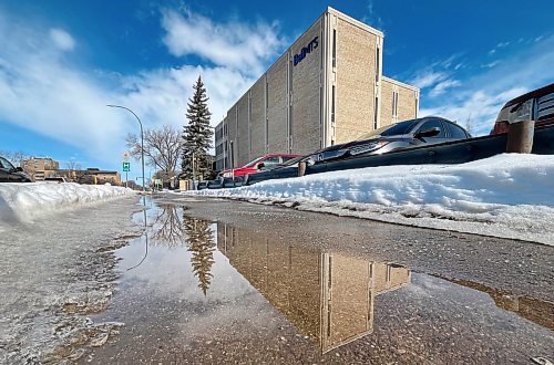 Meltwater on the sidewalk reflects Brandon's BellMTS building on 18th Street on Monday afternoon. (Matt Goerzen/The Brandon Sun)