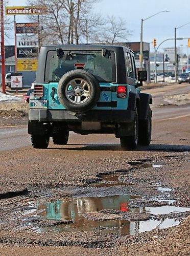 A jeep moves around a line of water-filled potholes on Richmond Avenue on Tuesday afternoon. (Matt Goerzen/The Brandon Sun)