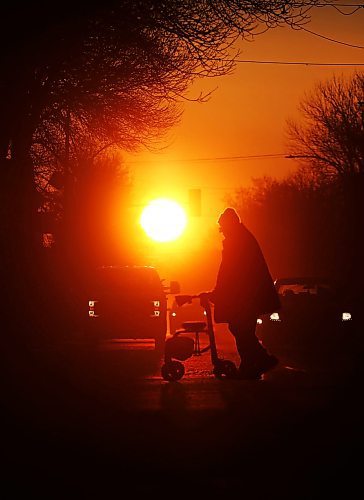 Silhouetted against the rising sun on the first day of spring, motorists wait at a stop light along Princess Avenue while a man with a walker crosses the street on Wednesday morning. (Matt Goerzen/The Brandon Sun).