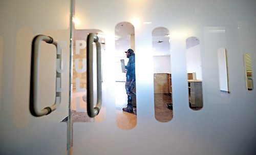 Seen through the front doors of the future home of Brandon's Food Rescue Grocery Store, Donovan Kimball, the store's logistics support, wields a drywall trowel as he helps ready the store for it's April 3 opening on Thursday afternoon. (Matt Goerzen/The Brandon Sun)
