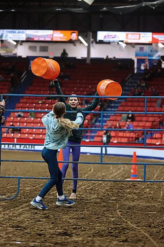 Aubree Swain and Sophie Vodon climb a metal gate carrying buckets as part of the Provincial Ex of Manitoba Youth Obstacle Course on Wednesday during the Royal Manitoba Winter Fair evening show. (Matt Goerzen/The Brandon Sun)