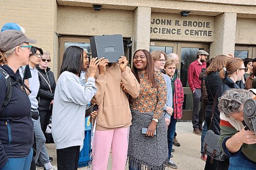 Three BU students peer into a solar-filtered portable telescope outside the Brodie Science Building at BU to see the partial eclipse on Monday afternoon in Brandon. (Michele McDougall/The Brandon Sun)