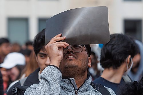 MIKE DEAL / FREE PRESS
Mechanical Engineering student, Chironton Swanon, uses an old X-ray film to see the partial eclipse. 
Students gather at the University of Manitoba to watch the partial solar eclipse during an overcast Monday afternoon.
240408 - Monday, April 08, 2024.