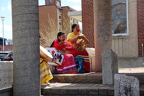 Drum performers listen to a speaker on Red Dress Day at Princess Park. (Charlotte McConkey/The Brandon Sun)