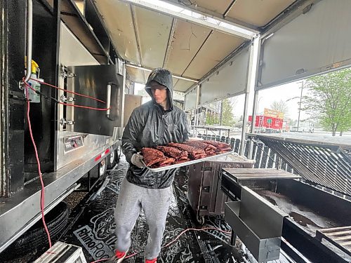 Merrick O’Mara, a backhouse supervisor with Blazin' BBQ, moves a platter of ribs from the smoker on Friday afternoon, as snow falls just outside the food trailer canopy. (Matt Goerzen/The Brandon Sun)