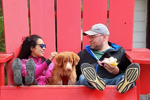 Parisa Jiwa and Keegan Hill-Mann enjoy a sundae together in an oversized Adirondack chair with their dog Ender while visiting Wasagaming in Riding Mountain National Park from Calgary with family on Thursday. (Tim Smith/The Brandon Sun)