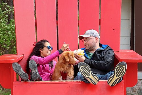 06062024
Parisa Jiwa and Keegan Hill-Mann enjoy a sundae together in an oversized Adirondack chair with their dog Ender while visiting Wasagaming in Riding Mountain National Park from Calgary with family on Thursday. 
(Tim Smith/The Brandon Sun)