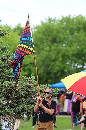 A man at Pride in the Park wearing rainbow face paint holds aloft a flag adorned with rainbow hearts on Saturday. (Colin Slark/The Brandon Sun)